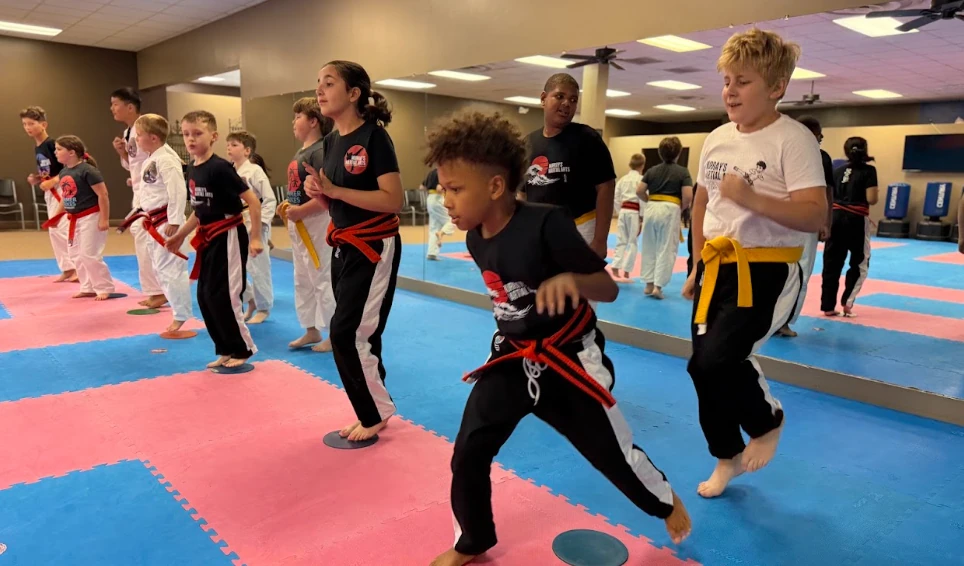 Children practicing footwork and balance drills on padded mats at Greece NY karate dojo.