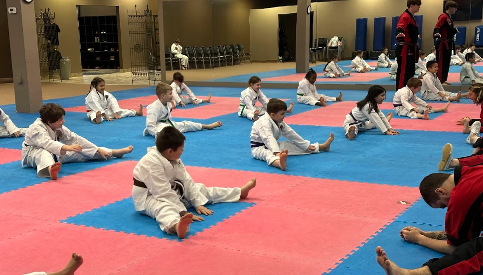 Kids doing flexibility stretching on safe mats at Murray's Martial Arts in Greece, NY.