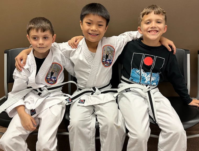 Three young karate students smiling together during class at Murray's Martial Arts in Greece, NY.